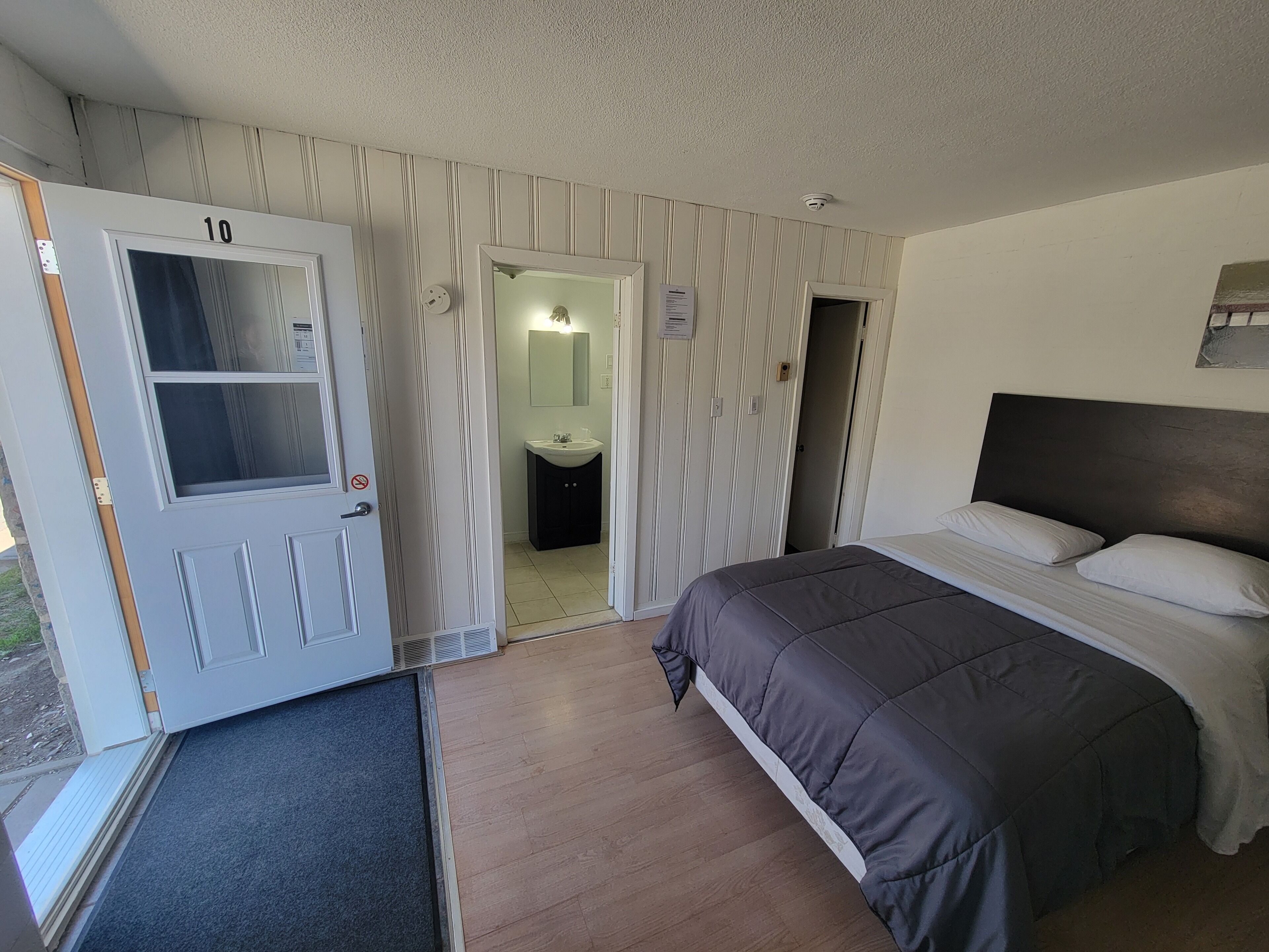 Une chambre avec un lit, une porte portant un numéro, une salle de bain avec un miroir et des toilettes.