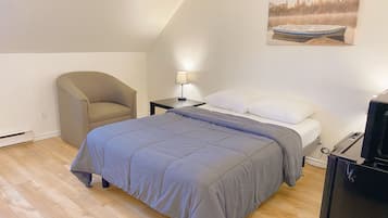 Ein Schlafzimmer mit einem Bett, einem Sessel, einem Schreibtisch mit Lampe und einem Fernseher.