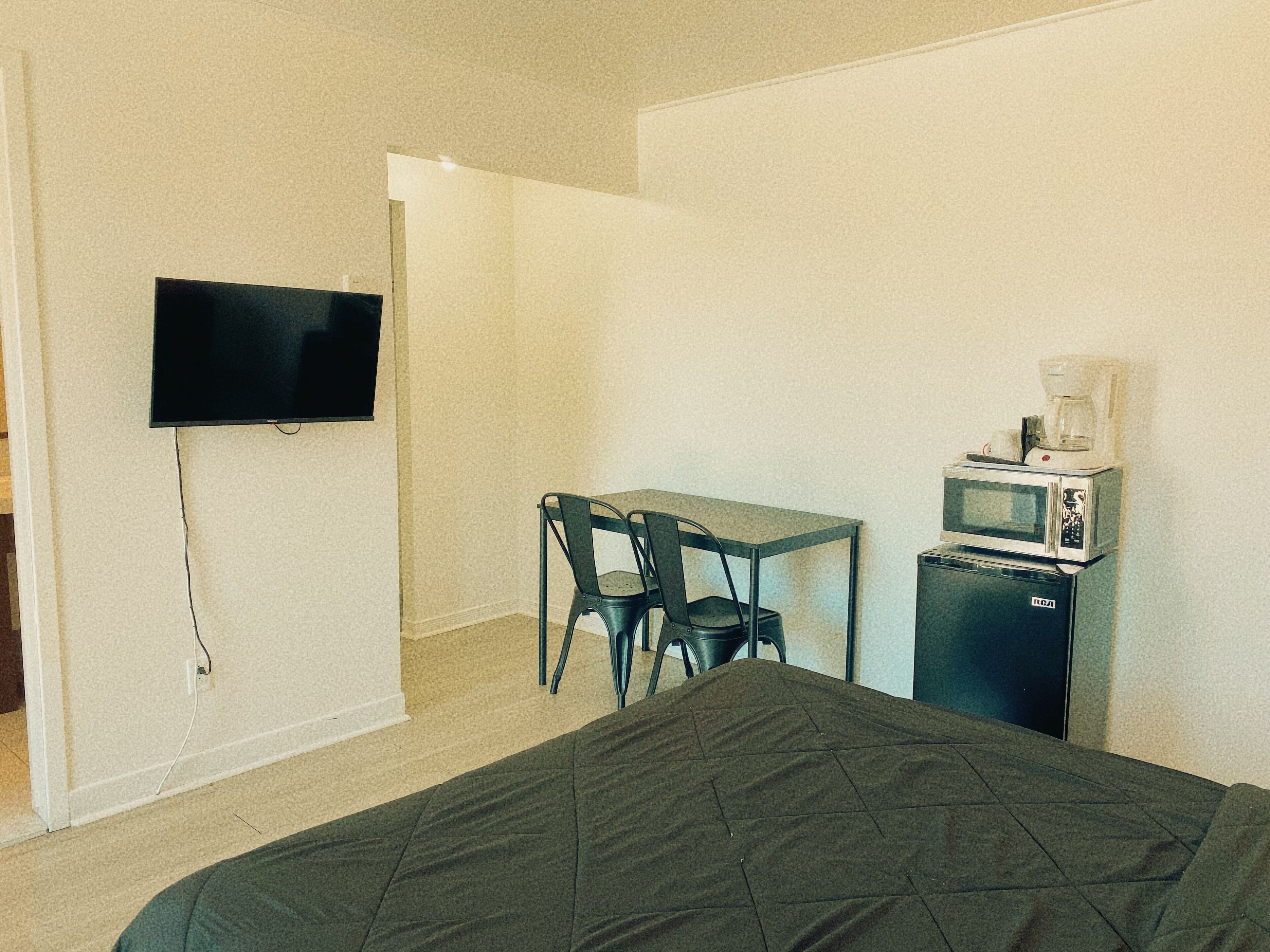 Une chambre avec un lit, un téléviseur fixé au mur, une petite table avec une chaise et un micro-ondes posé sur un meuble.