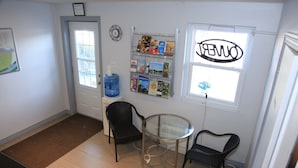 A room with a door, a water dispenser, a glass table, two chairs, a bulletin board with various items, and a window with a sign. - Motel Grande ile (Salaberry De Valleyfield)