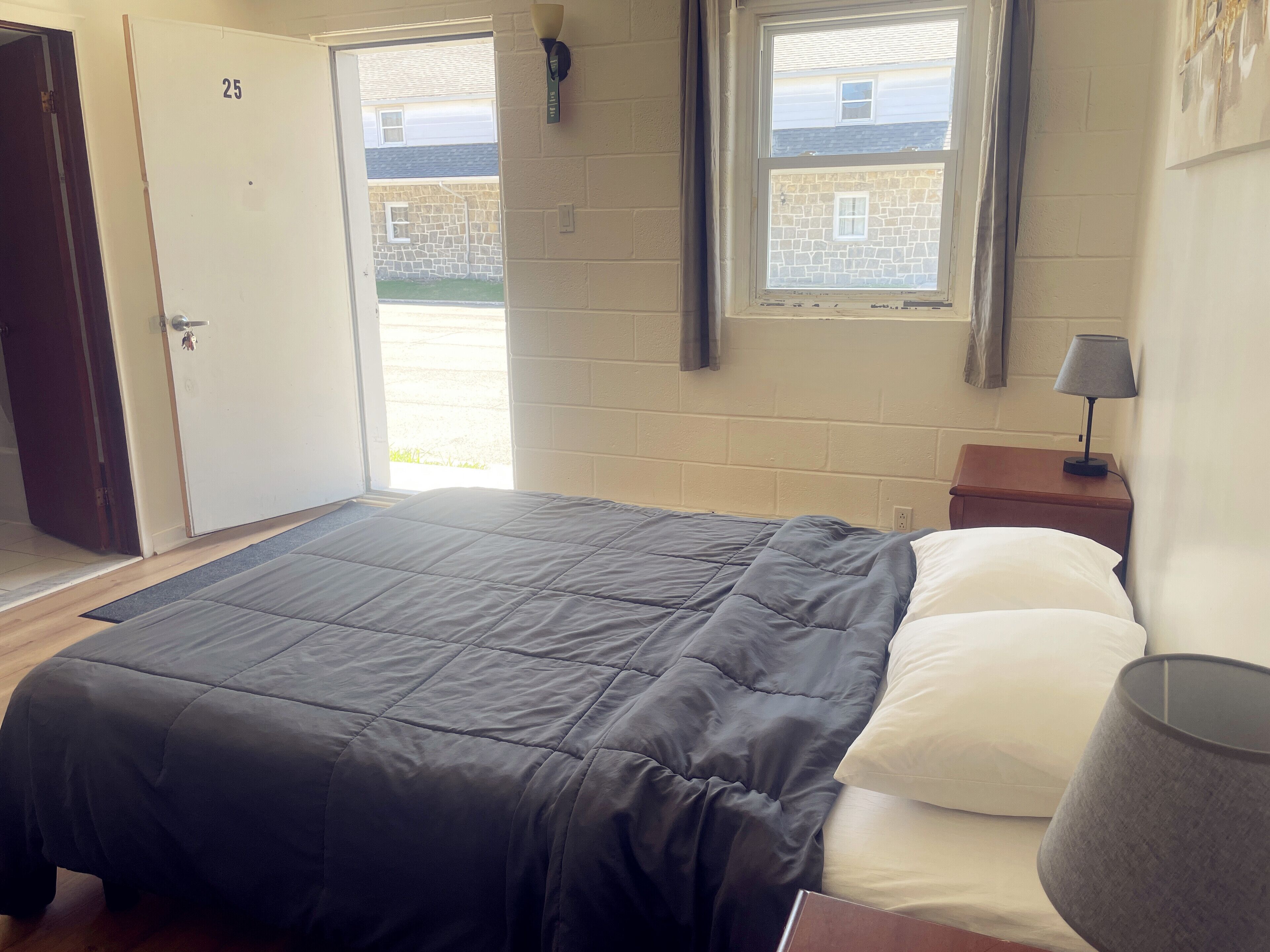 Un dormitorio con cama, mesita de noche, lámpara y puerta que da a un espacio exterior.