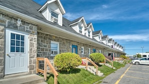 A row of stone buildings with white trim and blue shutters, each with a numbered door. - Motel Grande ile (Salaberry De Valleyfield)
