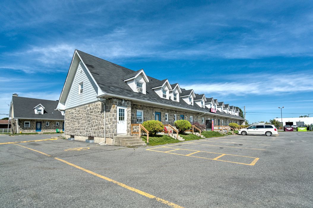Une rangée de bâtiments en pierre, avec un parking devant.