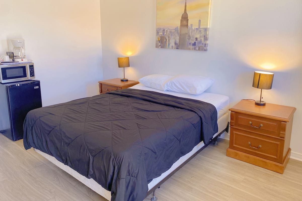 A hotel room with a bed, two bedside tables with lamps, a small wooden dresser, a microwave, and a coffee maker.