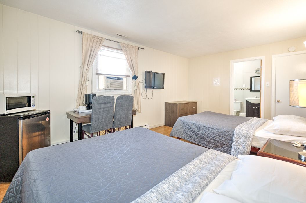 A hotel room with two beds, a desk with a chair, a microwave, a TV, and a small kitchenette.