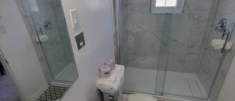 Un baño con ducha de mampara, inodoro, lavamanos y espejo.