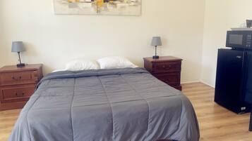 Un dormitorio con una cama grande, dos mesitas de noche con lámparas, un aparador, un microondas y un cuadro en la pared.