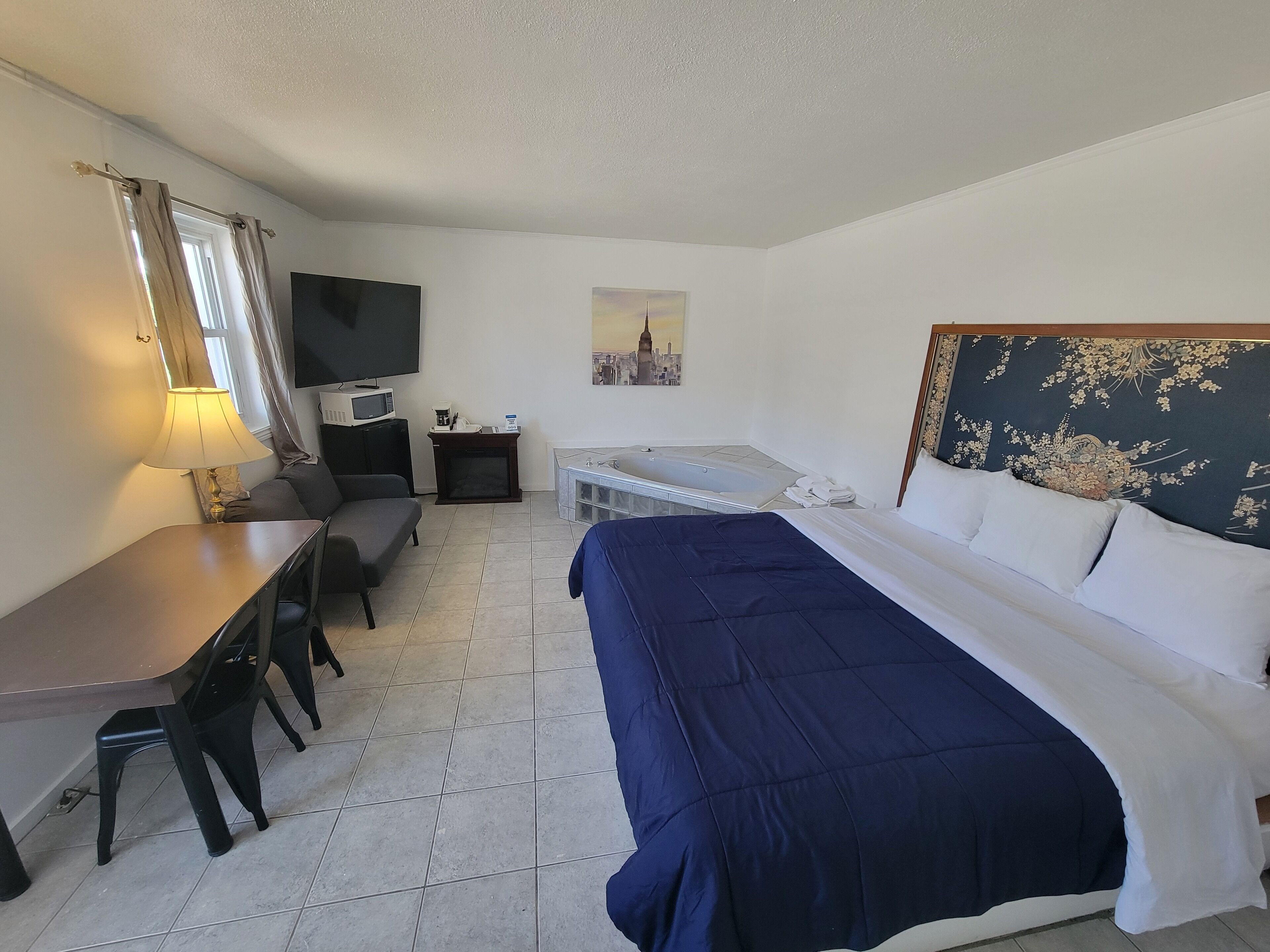 Une chambre d’hôtel équipée d’un lit, d’un bureau, d’une chaise, d’une télévision, d’une petite table avec une machine à café et d’un tableau représentant un paysage urbain.