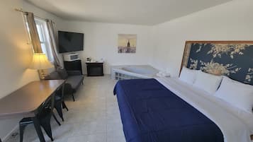 Une chambre d’hôtel équipée d’un lit, d’un bureau, d’une chaise, d’une télévision, d’une petite table avec une machine à café et d’un tableau représentant un paysage urbain.