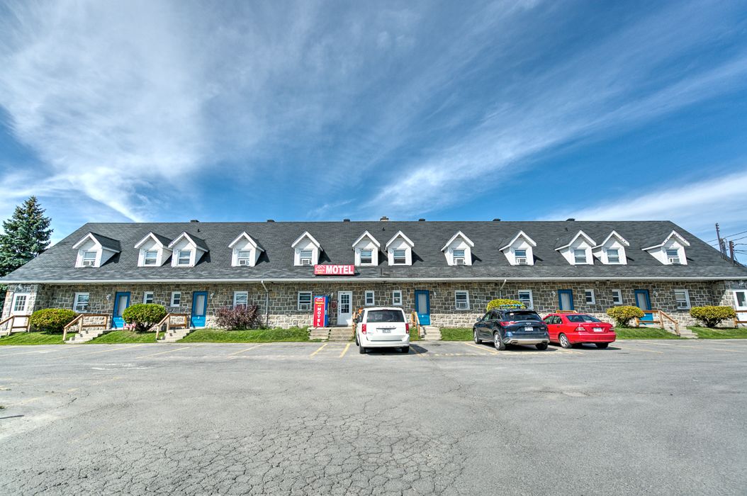 A motel with a row of rooms, a parking lot, and a clear blue sky.