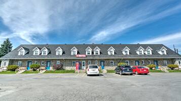 A motel with a row of rooms, a parking lot, and a clear blue sky.