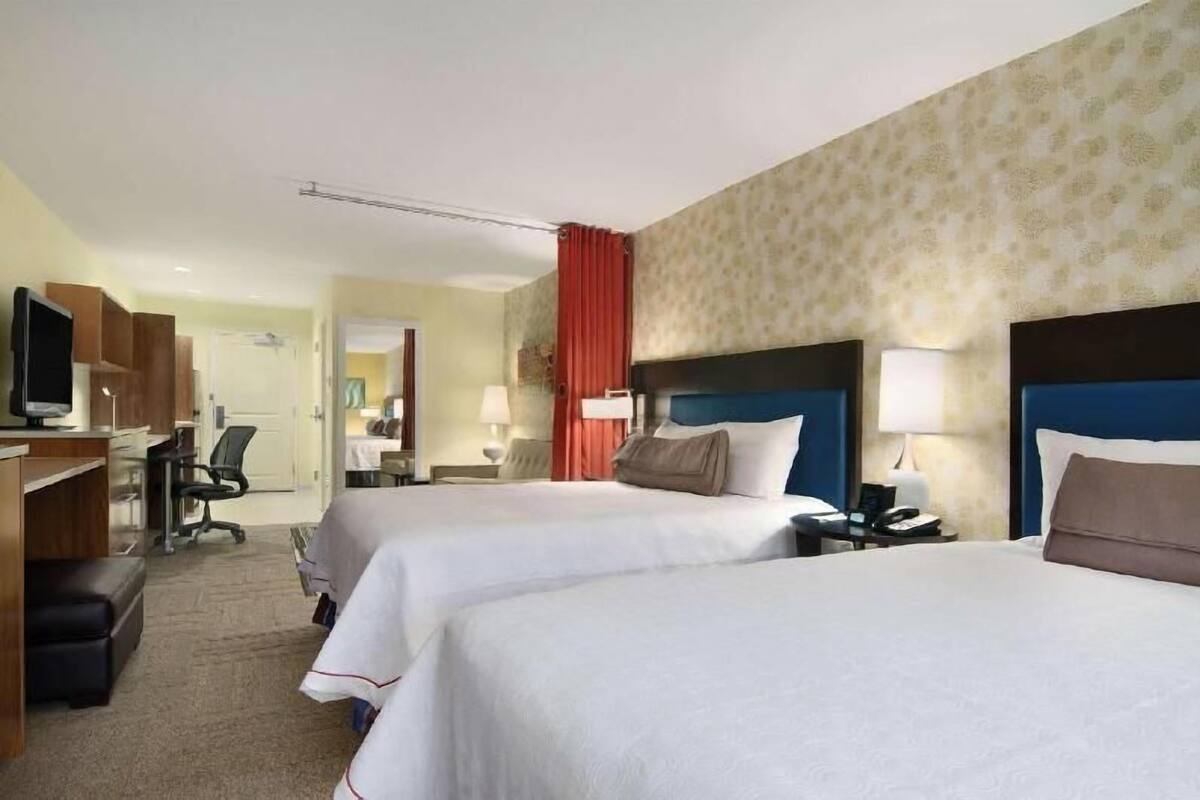 A hotel room with two beds, a desk with a computer, a chair, and a TV.