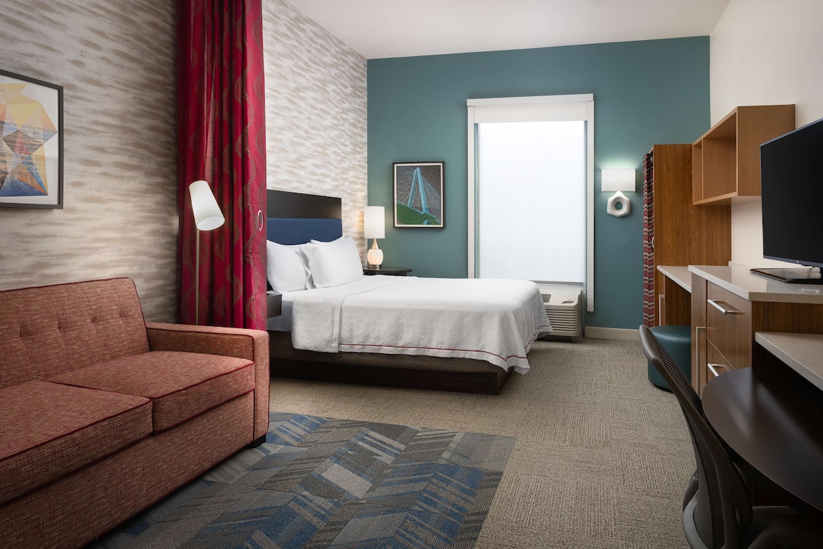 A hotel room with a bed, a sofa, a desk, and a television.