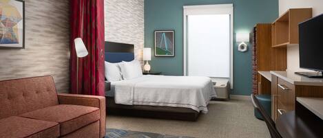 A hotel room with a bed, a sofa, a desk, and a television.