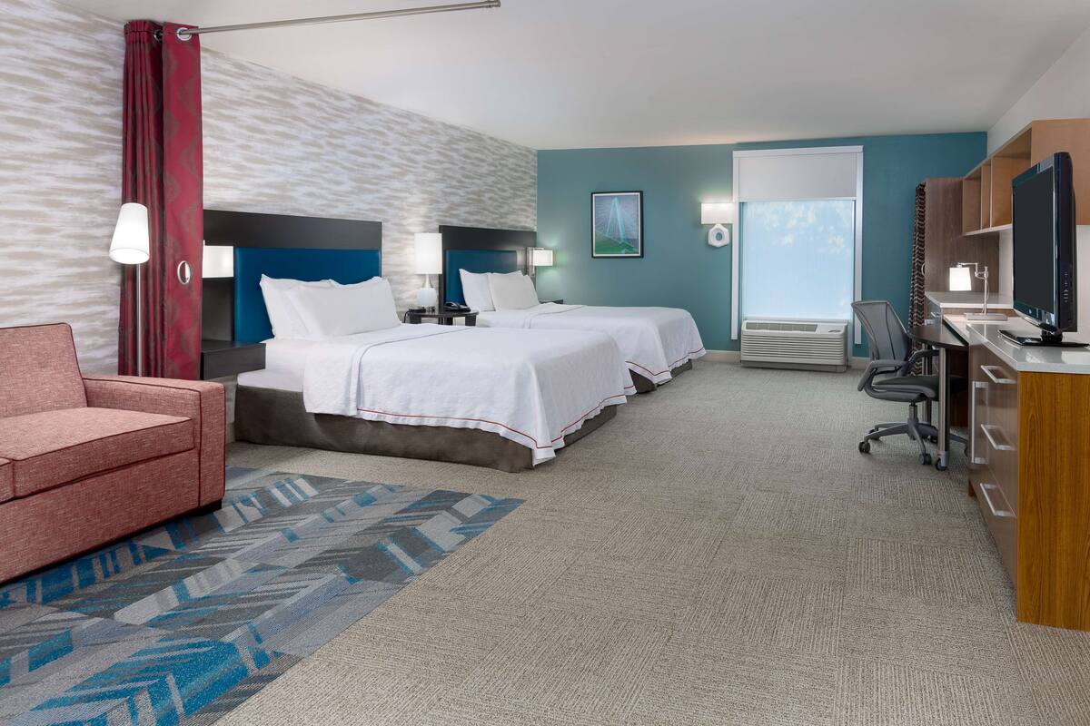 A hotel room with two beds, a desk with a computer, a TV, a chair, and a couch.