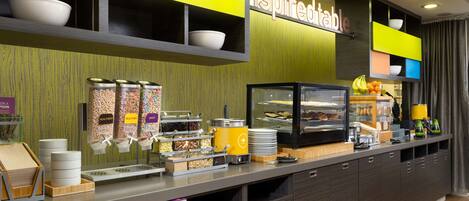 Een ontbijtbuffet met gemarkeerde voedselcontainers, een glazen vitrine en een bord met de tekst 'Goedemorgen'.