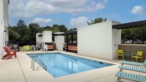 Une piscine entourée de chaises longues et de tables, ainsi que d’un espace de repos couvert et d’un bâtiment.