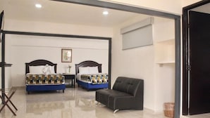 Habitación de hotel con dos camas, un sofá, un televisor y suelo de baldosas.