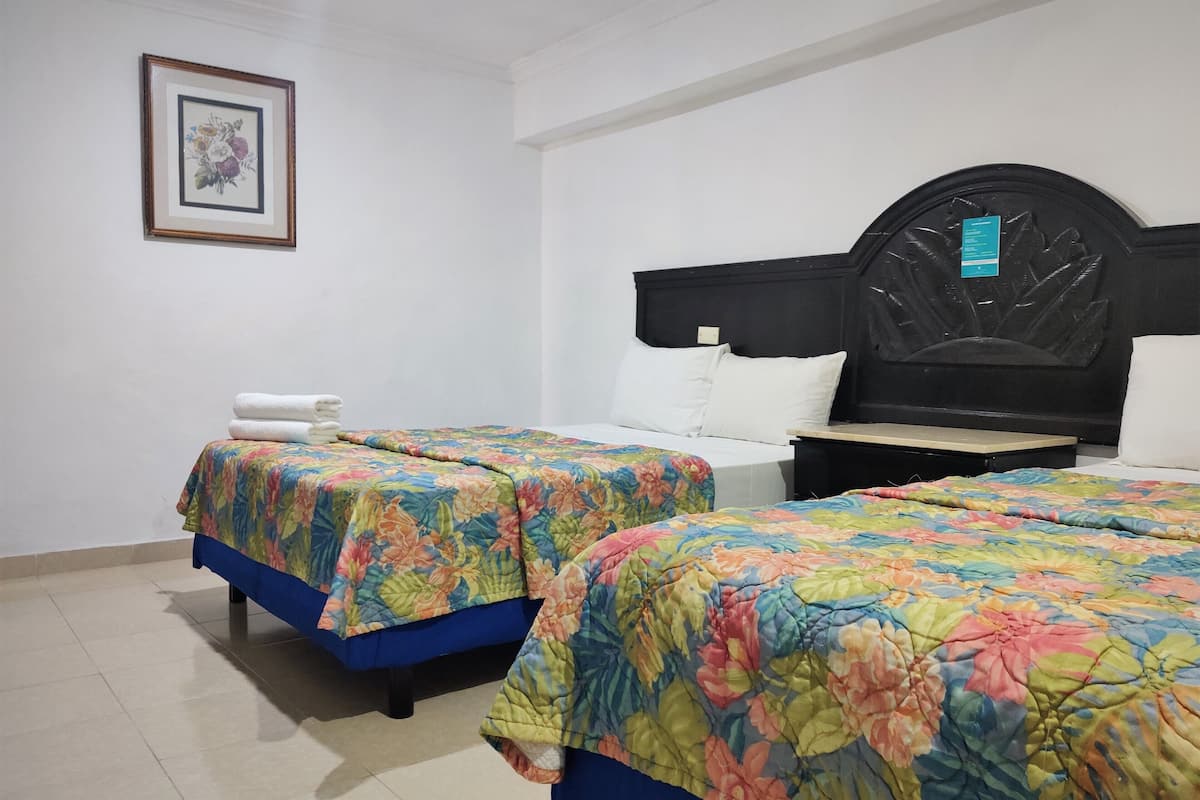 A hotel room with two beds, each with a floral bedspread, a bedside table with a lamp, and a framed picture on the wall.