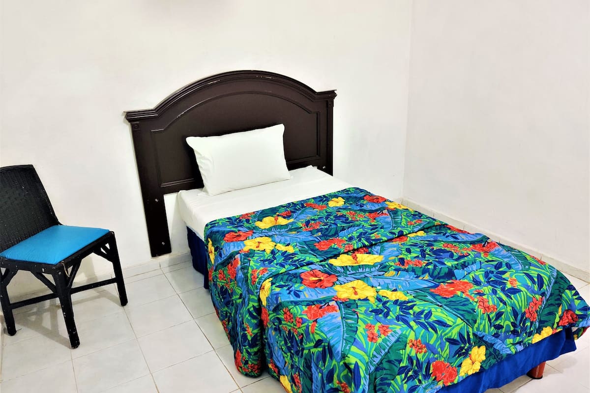 A bed with a floral bedspread, a black upholstered chair, and a white pillow.