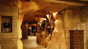 A stone-walled hallway with a wooden cabinet and a hanging sign. - Pirates Village (Calvia)