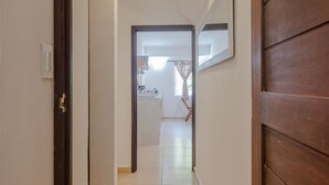 A hallway with a wooden door on the right, a mirror on the wall, and a view into a room with a window and curtains. - Villas Picalu Lodge (Puerto Aventuras)