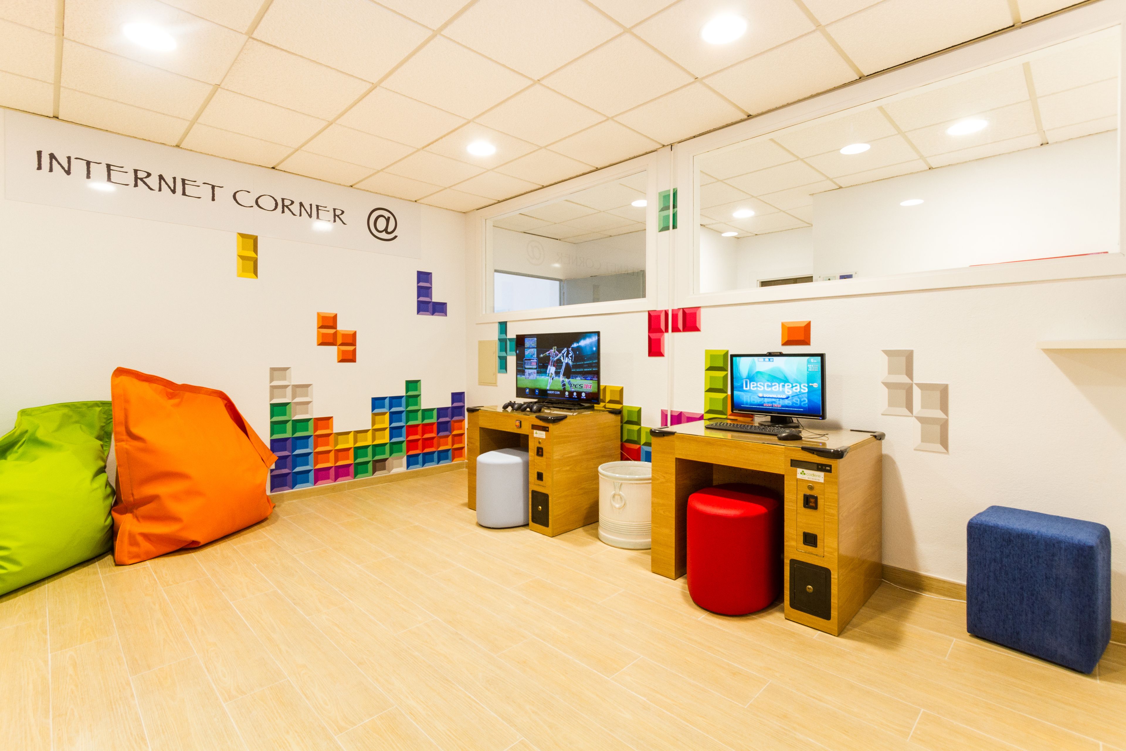 Um espaço de trabalho moderno com duas mesas, cubos de armazenamento coloridos e uma placa com a inscrição 'INTERNET CORNER'.
