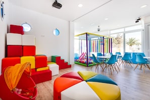 A brightly lit room with colorful seating, a play area, and large windows. - Plazamar Serenity Resort (Calvia)