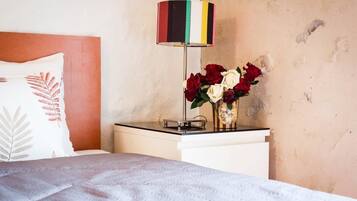 A neatly made bed with a white pillow featuring a fern design, a bedside table with a striped lamp, and a vase with red and white roses.