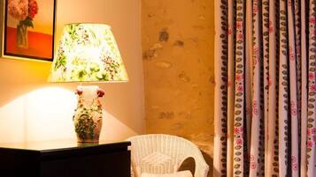 A room with a lamp, a vase with flowers, a wicker chair, and patterned curtains.