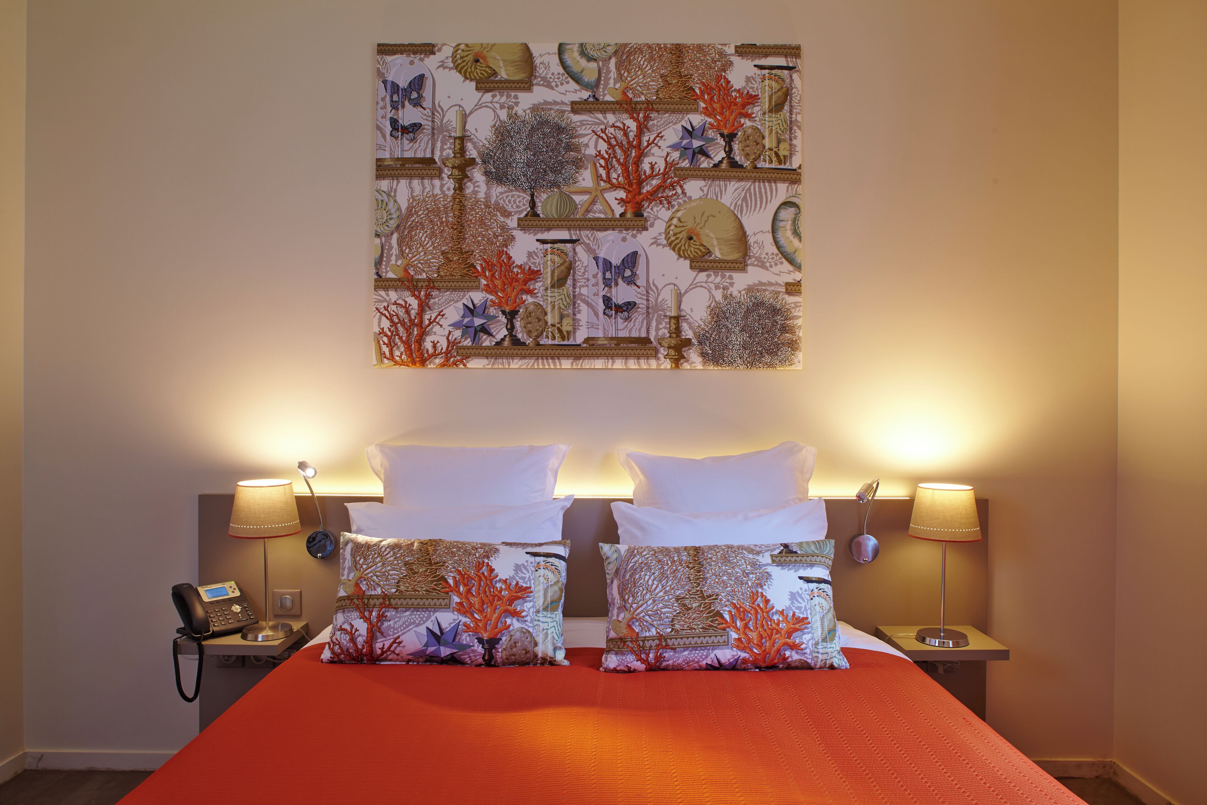 Una habitación de hotel con una cama, dos mesitas de noche, un teléfono y una obra de arte en la pared.