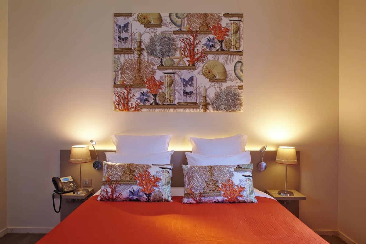 Una habitación de hotel con una cama, dos mesitas de noche, un teléfono y una obra de arte en la pared.
