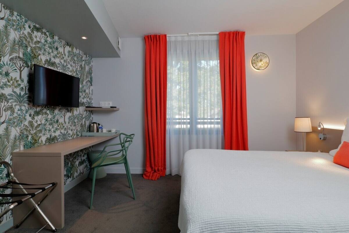 Ein Hotelzimmer mit Bett, Schreibtisch mit Stuhl, Fernseher und einem Fenster mit Vorhängen.