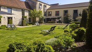A courtyard with a lawn, seating area, and buildings with stone and plaster facades.