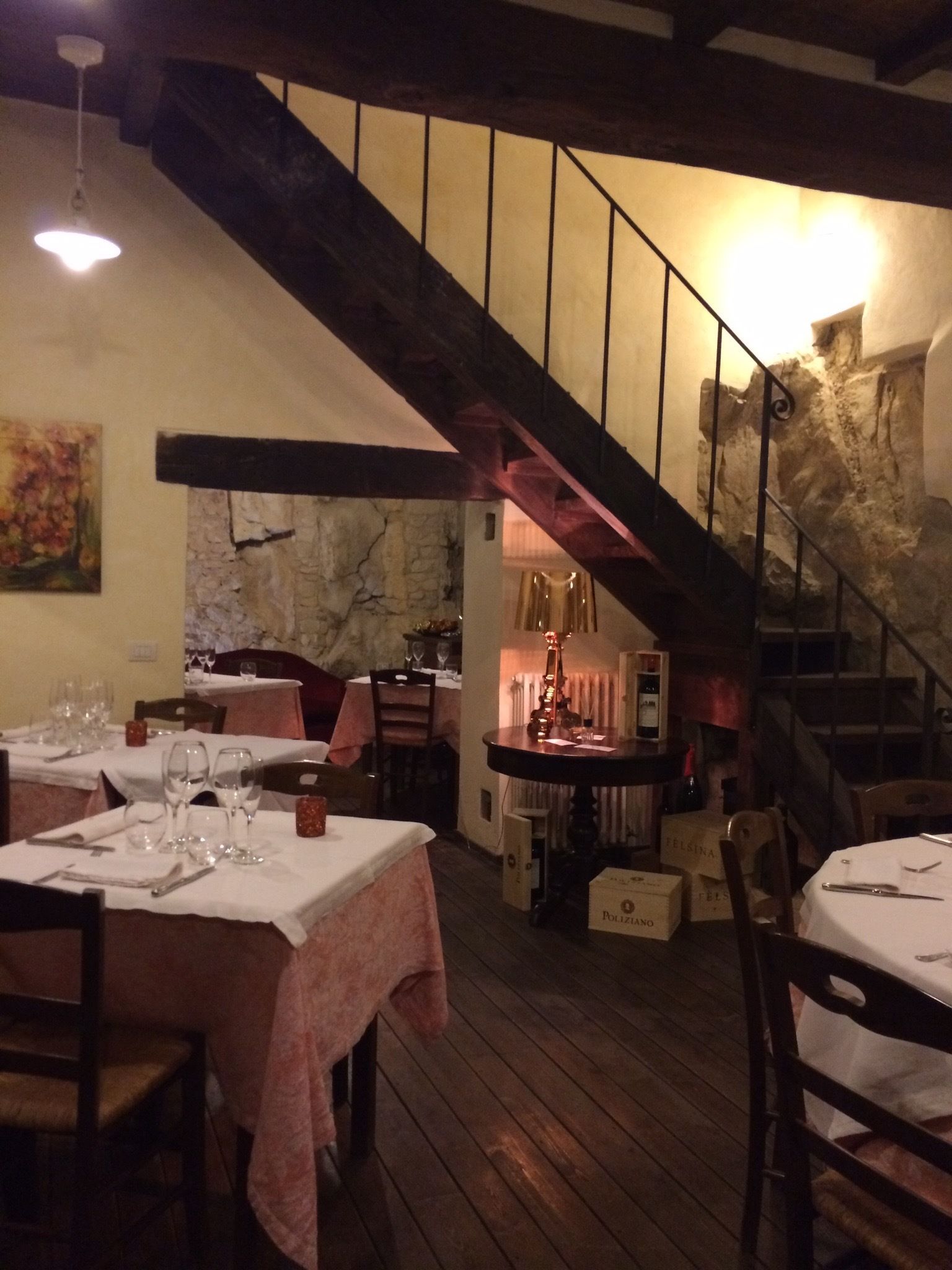 A restaurant with wooden floors, tables set for dining, a staircase, and a stone wall.