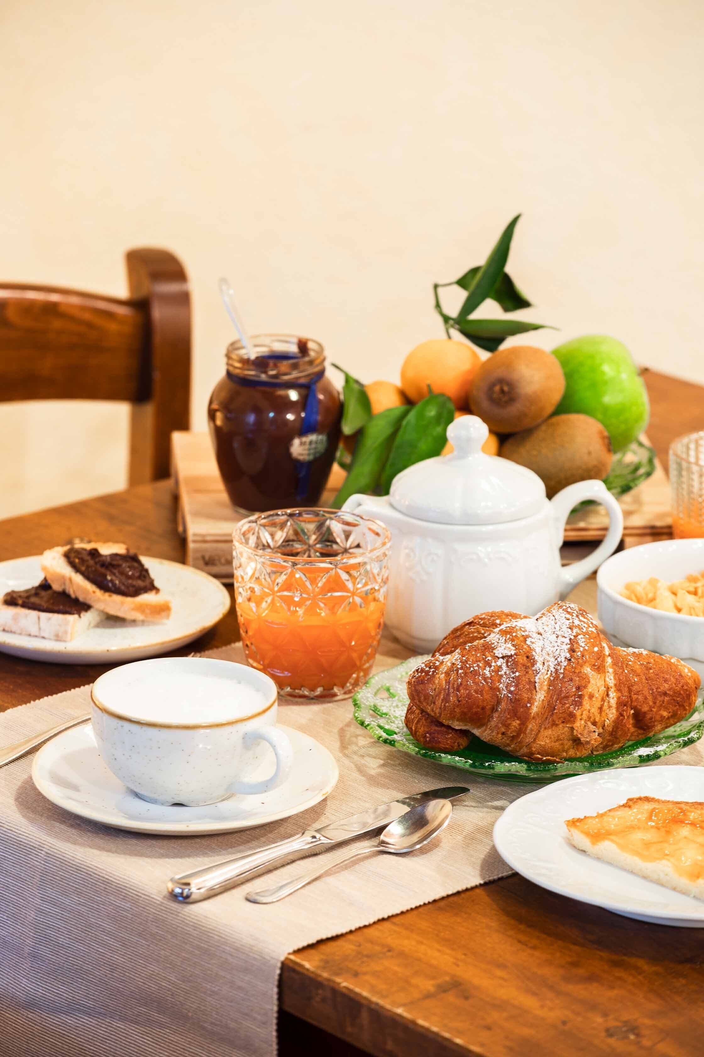 Desayuno con un croissant, café, jugo y diversas frutas sobre una mesa de madera.