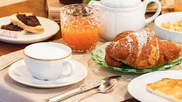 Desayuno con un croissant, café, jugo y diversas frutas sobre una mesa de madera.