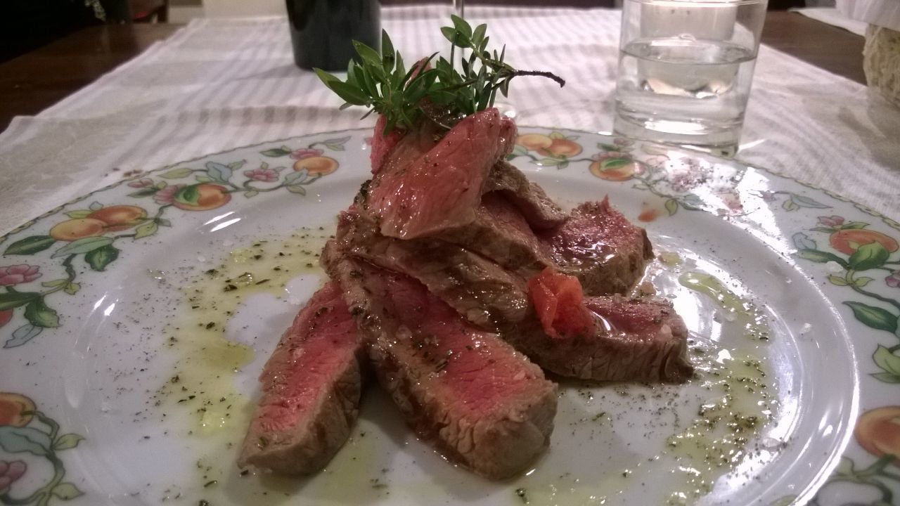 A plate of sliced steak with a sprig of herb on top, served on a floral-patterned plate.