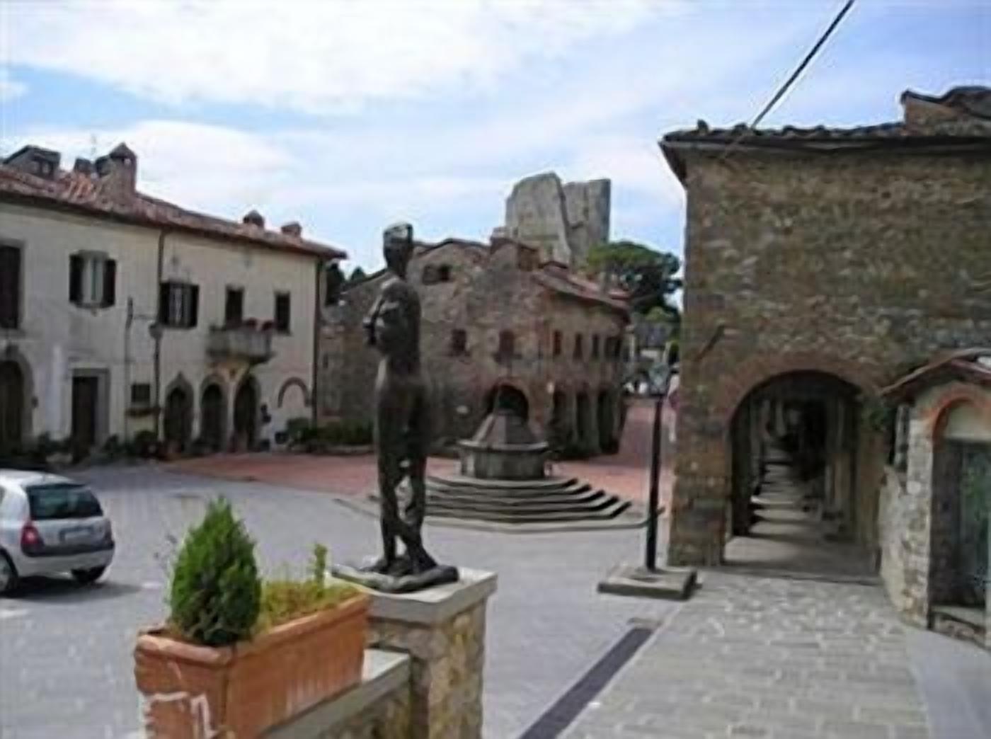 Una calle estrecha con edificios históricos de piedra, una estatua y una fuente.