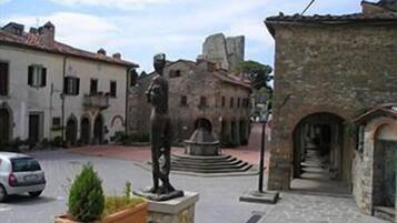 Una calle estrecha con edificios históricos de piedra, una estatua y una fuente.