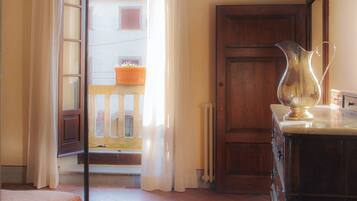 A room with a bed, a dresser, a wooden door, and a view of a building outside.