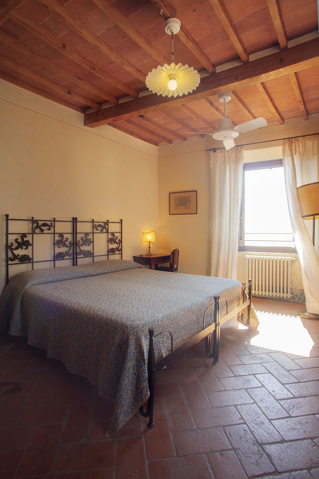 Ein Schlafzimmer mit Bett, Schreibtisch, Stuhl, Heizkörper und einem Fenster mit Vorhängen.