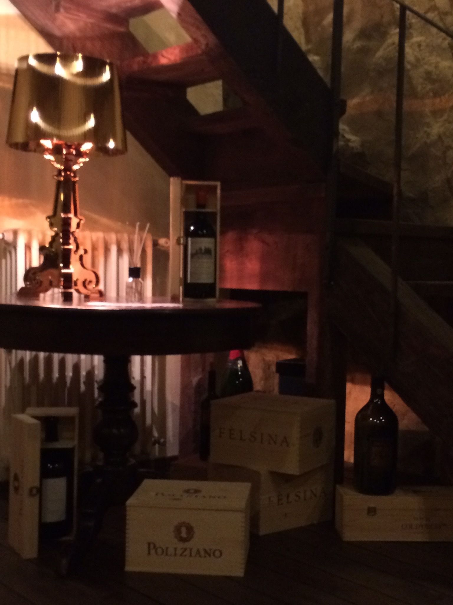 A dimly lit room with a table lamp, wooden beams, and boxes labeled 'Felsina' and 'Poliziano'.