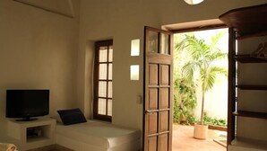 Ein Zimmer mit Bett, Fernseher, Fenster und einer Tür, die auf einen Balkon mit Pflanzen führt.