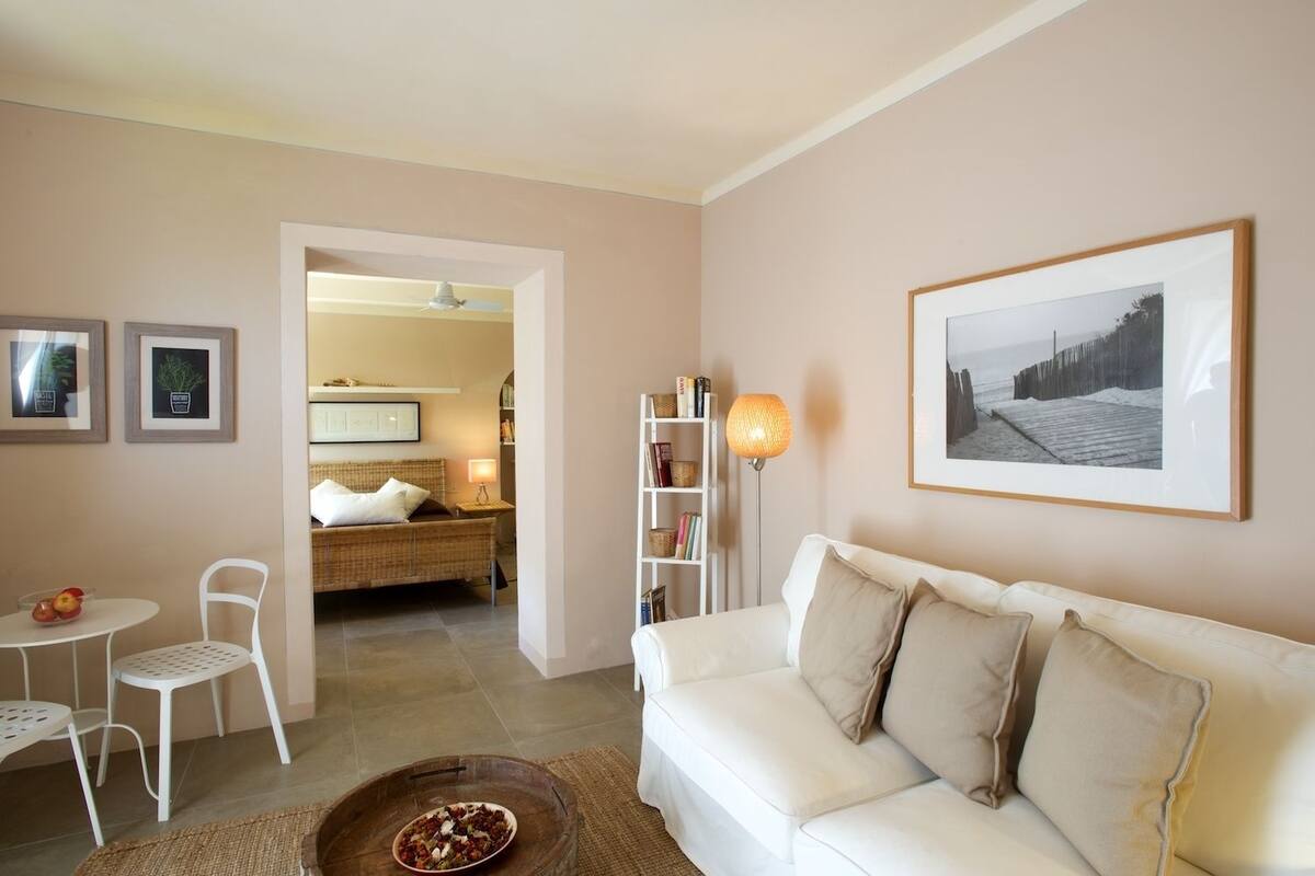 Un salon avec un canapé blanc, une table à manger avec des chaises, une bibliothèque et un tableau encadré au mur.