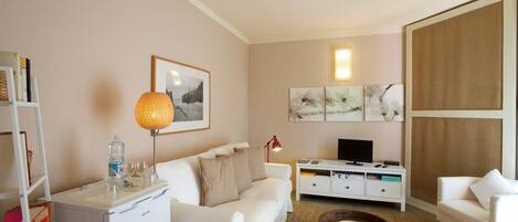 A modern living room with a white sofa, a coffee table, a TV on a white cabinet, and artwork on the wall.