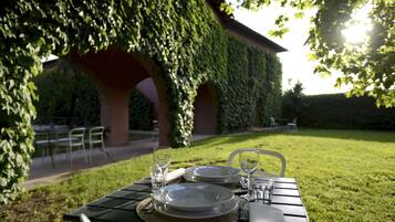 A table set outdoors with plates, glasses, and cutlery, under a structure covered with ivy.