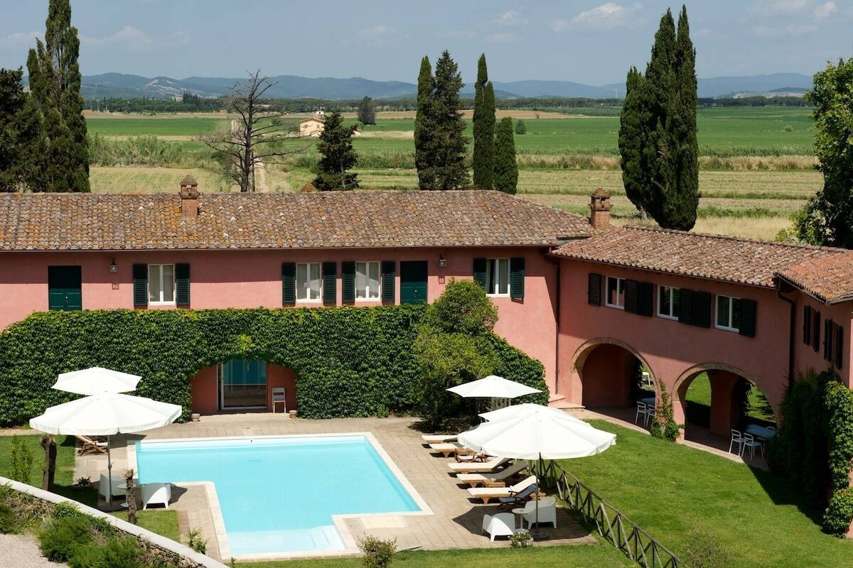 Une villa rose dotée d’une piscine, d’un espace salon extérieur et offrant une vue sur la campagne.