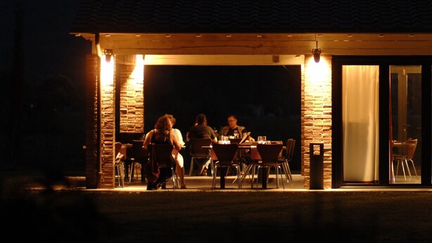 Un espacio comedor al aire libre cubierto con paredes de piedra y techo, con vistas a una colina iluminada.