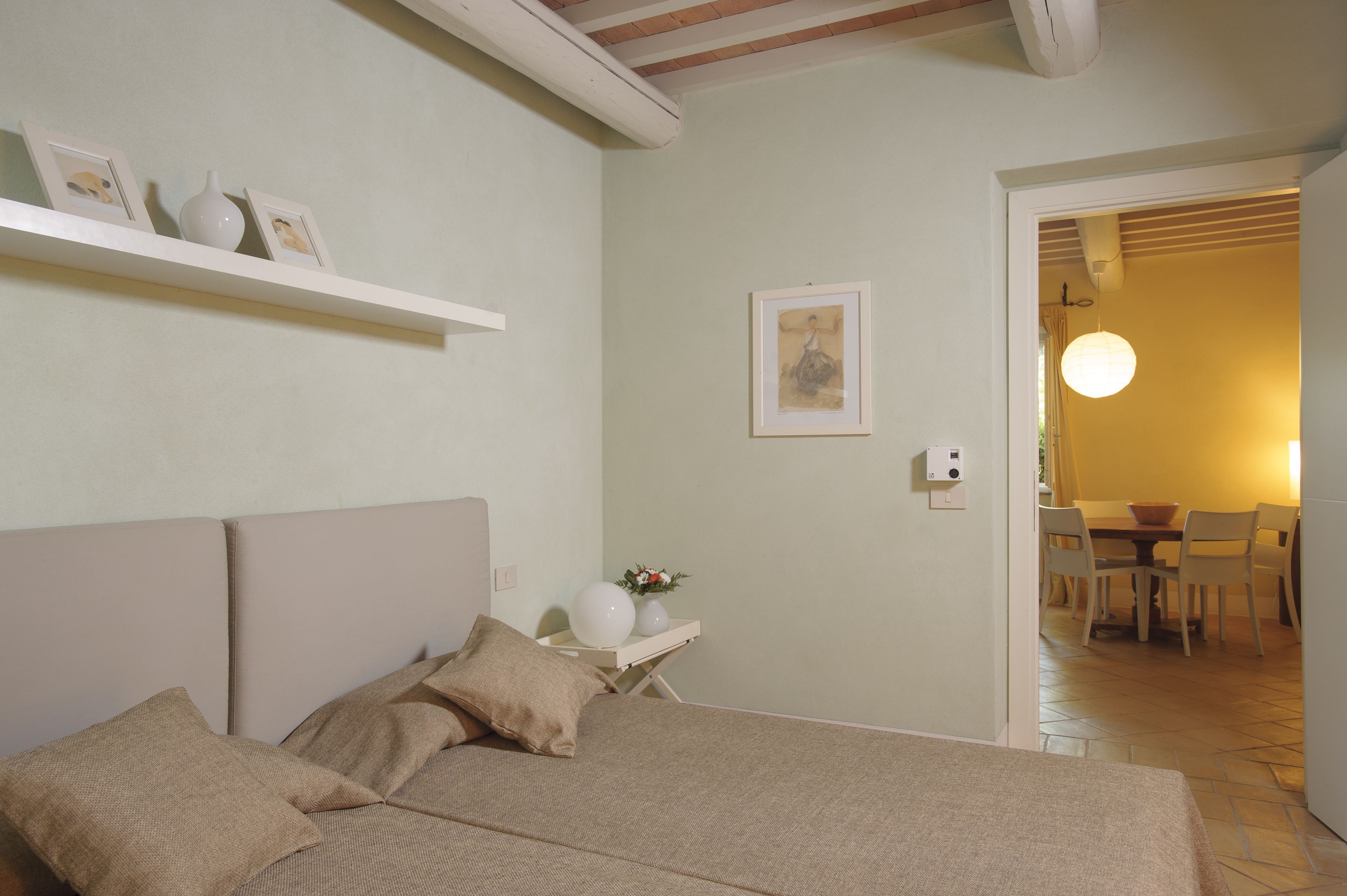 Un dormitorio con cama, mesita de noche y un estante blanco pequeño con fotos enmarcadas.